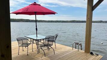 Une terrasse en bois avec une table et des chaises, un parasol rouge et une vue sur un lac.