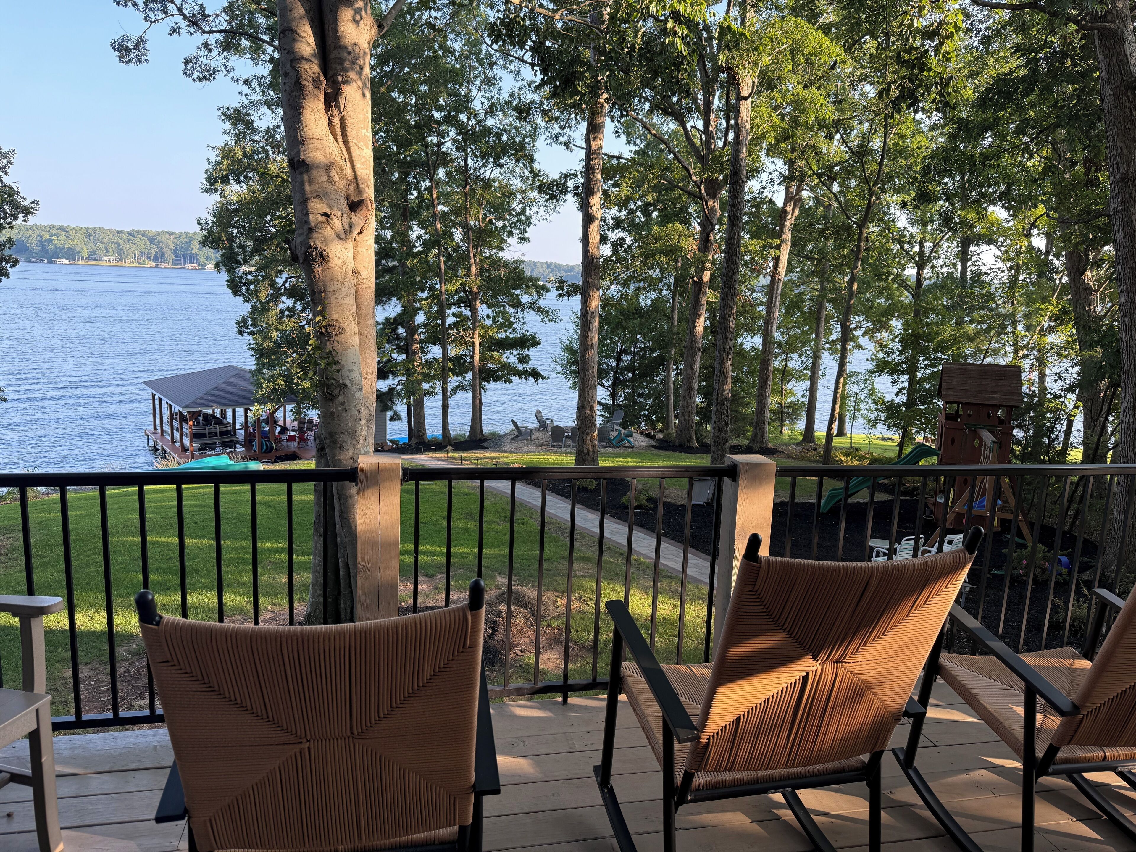 A deck with wicker chairs overlooking a lake, a gazebo, and a playground.