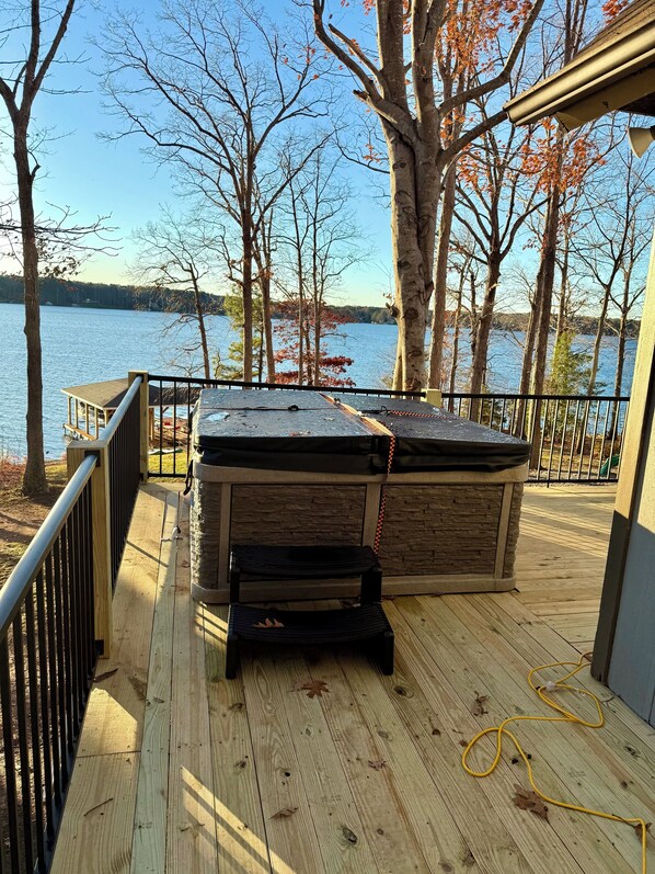 Une terrasse dotée d’un jacuzzi, d’un mur en pierre et offrant une vue sur un lac.