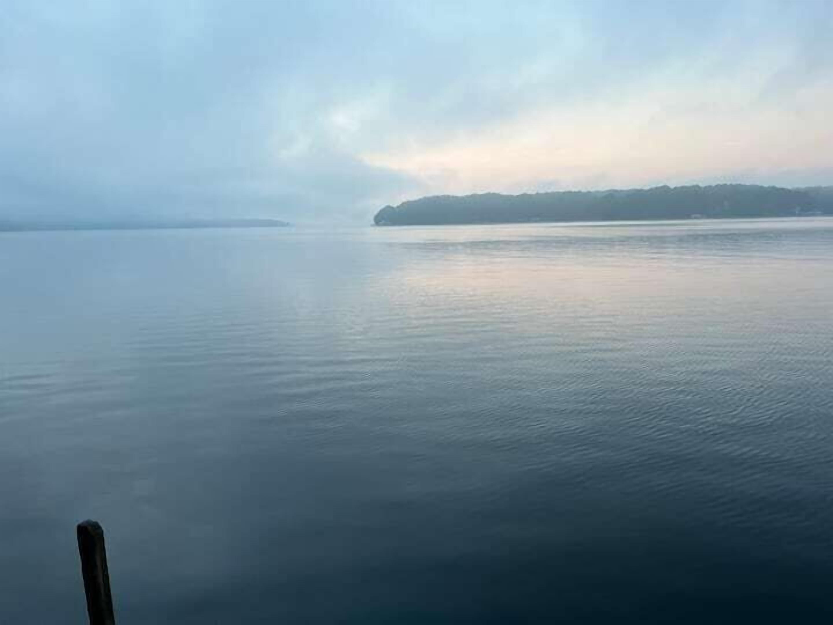 A calm body of water with a distant landmass and a cloudy sky.