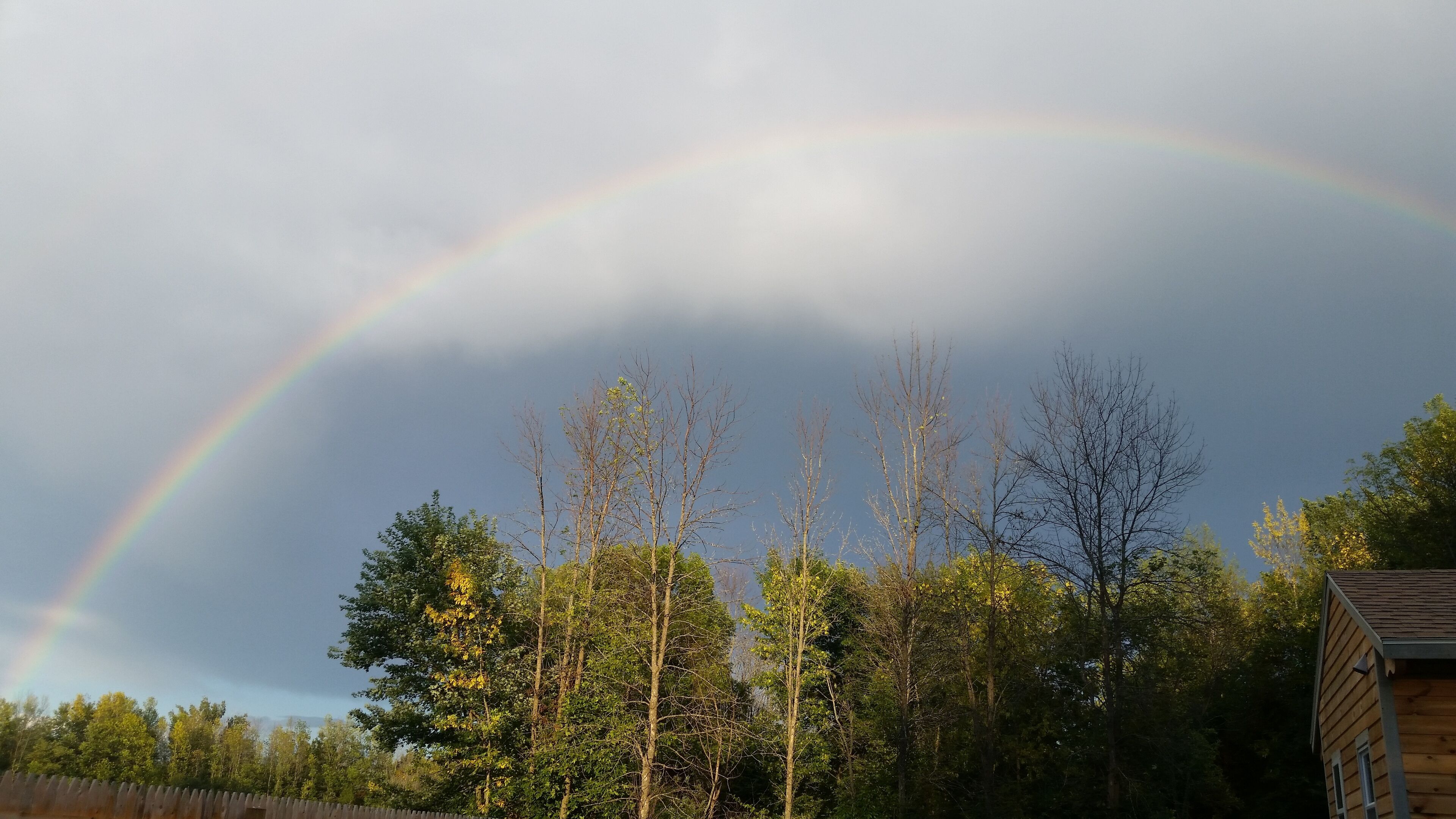 Eine Holzhütte mit Blick auf einen Regenbogen über einem bewaldeten Gebiet.