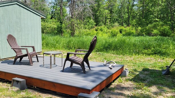 A wooden deck with two Adirondack chairs and a small table. - Lake Champlain Tiny House Paradise Private & Beautiful! (Alburgh)