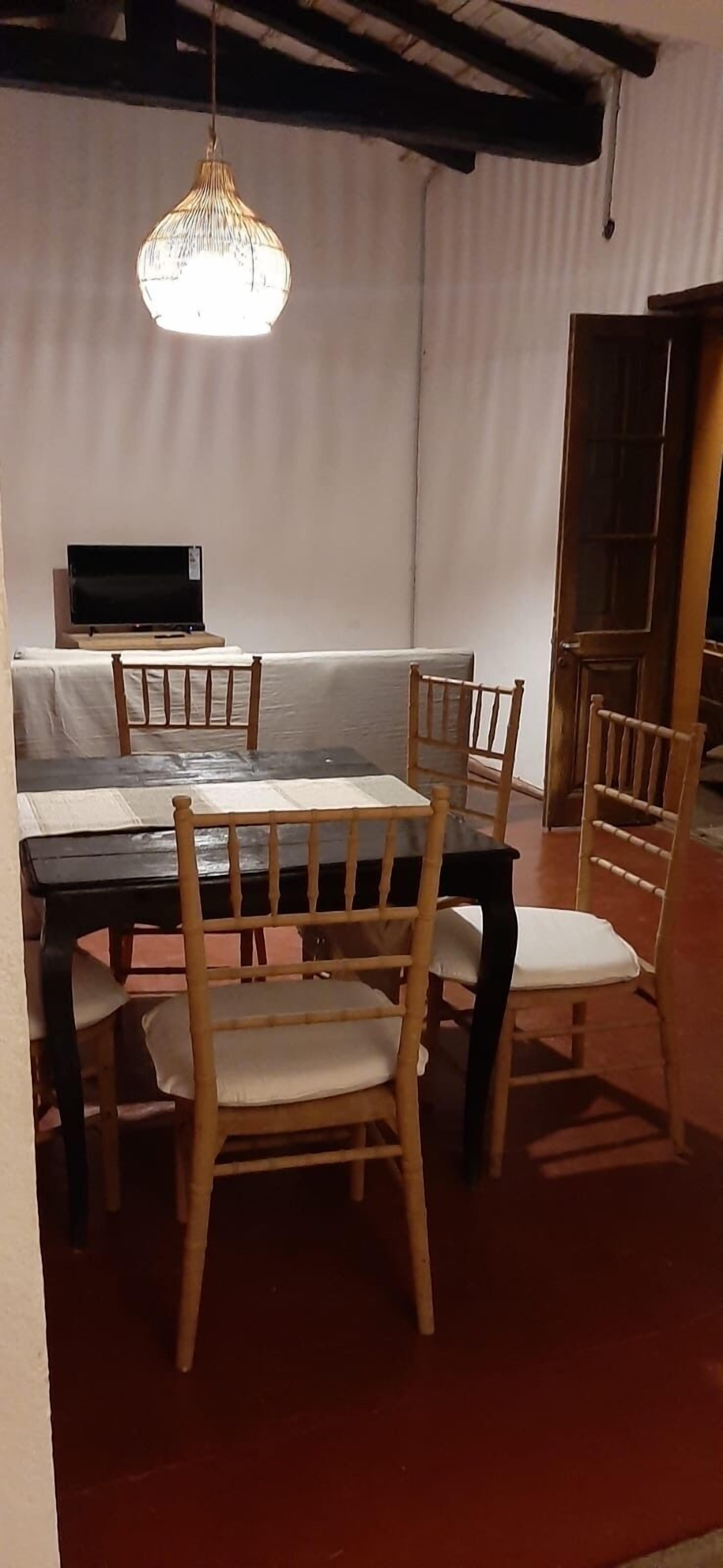 A dining area with a table and chairs, a hanging light fixture, and a television on a stand.