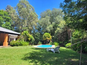 Un jardin avec une piscine, un fauteuil de relaxation et une végétation luxuriante.