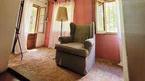 A room with a high ceiling, a single window, a chair, and a lamp.