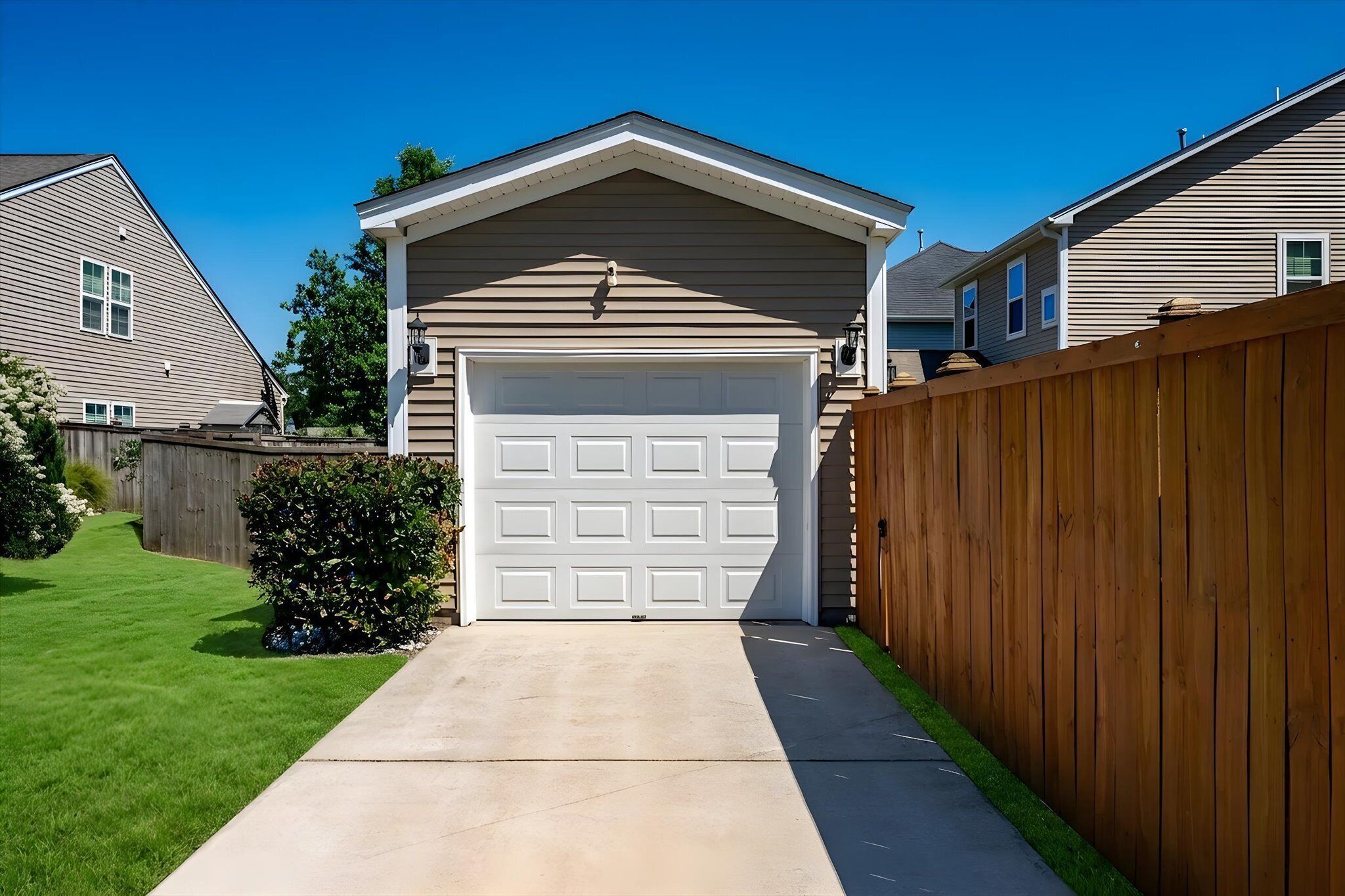 Un garage attenant à une maison, avec une clôture en bois, une allée en béton et une pelouse bien entretenue.