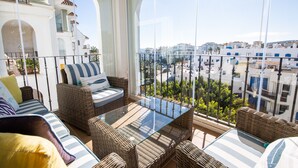 Ein Balkon mit Korbmöbeln, einem Glastisch und Blick auf Gebäude.