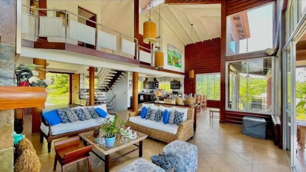 A spacious living area with a high ceiling, a staircase, and a kitchen visible in the background. - Fascinante rancho (personal de servicio incluido) (Jarabacoa)