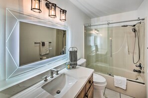 A modern bathroom with a large mirror, a sink, a toilet, and a glass-enclosed shower. - Hot Springs Vacation Rental w/ Game Room! (Hot Springs)