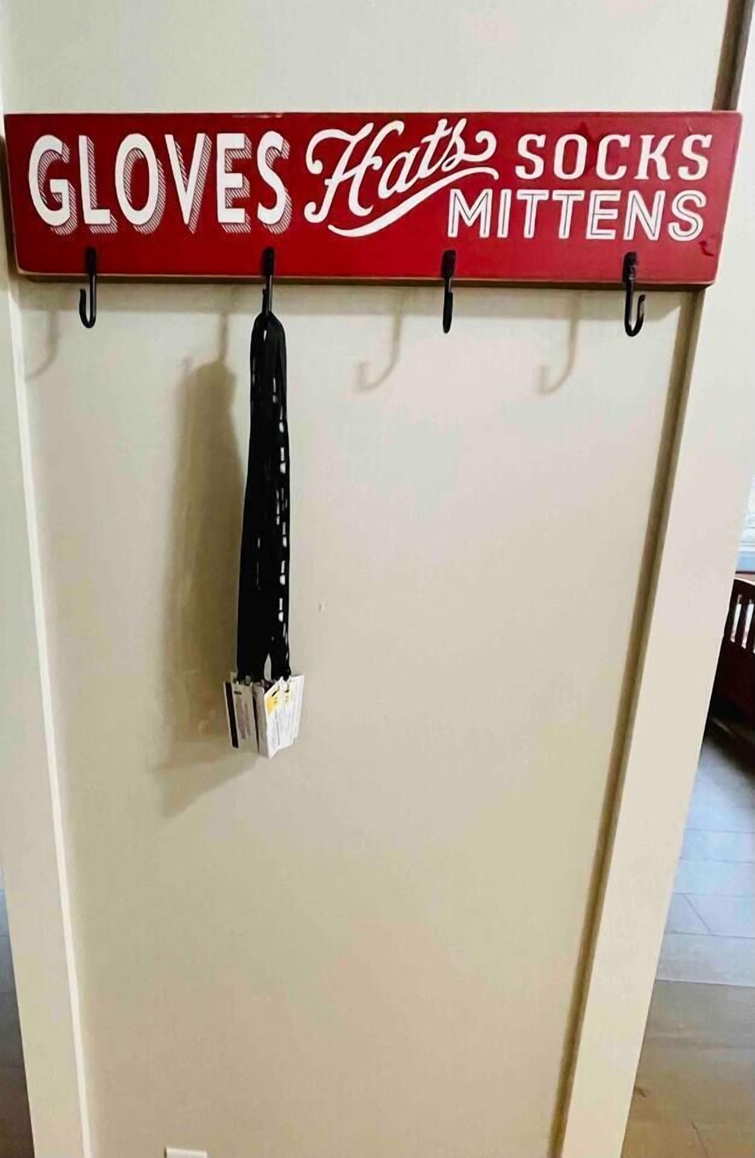 Um letreiro fixado na parede com os dizeres "GLOVES Hats Socks Mittens" e uma luva preta pendurada em um gancho.