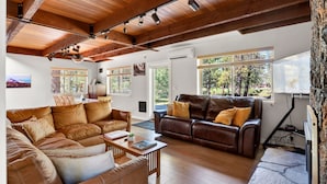 A spacious living area with leather sofas, wooden beams, and large windows offering views of the outdoors. - Walk to the Village, Hot Tub, SHARC pass, AC, Games, Bikes, Grill, Pet-Friendly (Sunriver)