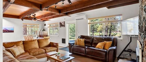 A spacious living area with leather sofas, wooden beams, and large windows offering views of the outdoors.