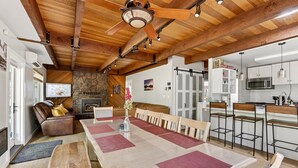 A spacious kitchen with a long dining table, wooden ceiling beams, and a stone fireplace. - Walk to the Village, Hot Tub, SHARC pass, AC, Games, Bikes, Grill, Pet-Friendly (Sunriver)