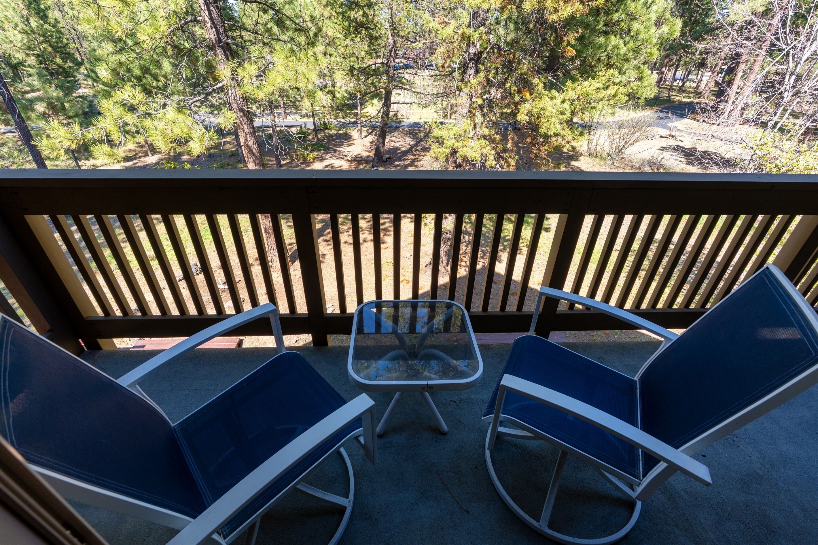 A balcony with two chairs and a table, overlooking a forested area.