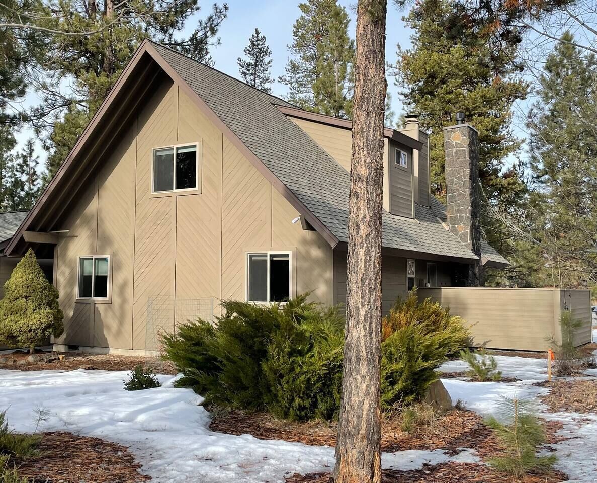 A two-story house with a sloped roof, a stone chimney, and a small front porch.