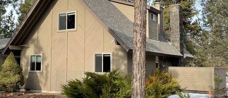 A two-story house with a sloped roof, a stone chimney, and a small front porch.