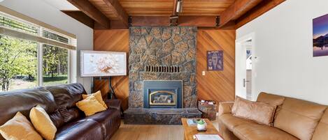 A living room with a stone fireplace, leather sofas, a wooden coffee table, and a view of the outdoors.