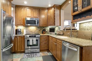 A modern kitchen with wooden cabinets, stainless steel appliances, granite countertops, and a built-in oven.