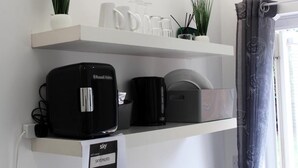 A kitchen area with a coffee maker, a kettle, and a dish rack on a white shelf.