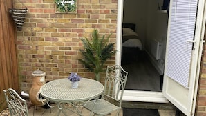 A patio with a round metal table and chairs, a potted plant, and a welcome sign on a brick wall.