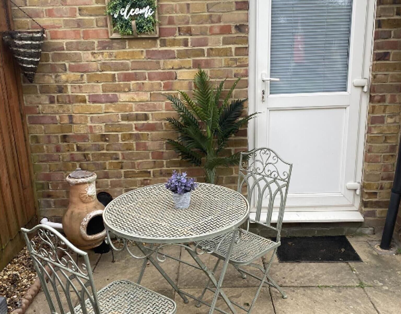 A round metal table with two chairs, a potted plant, and a decorative item on a brick wall.