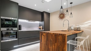 Une cuisine moderne avec des meubles de couleur sombre, un îlot central en bois et des tabourets de bar blancs.