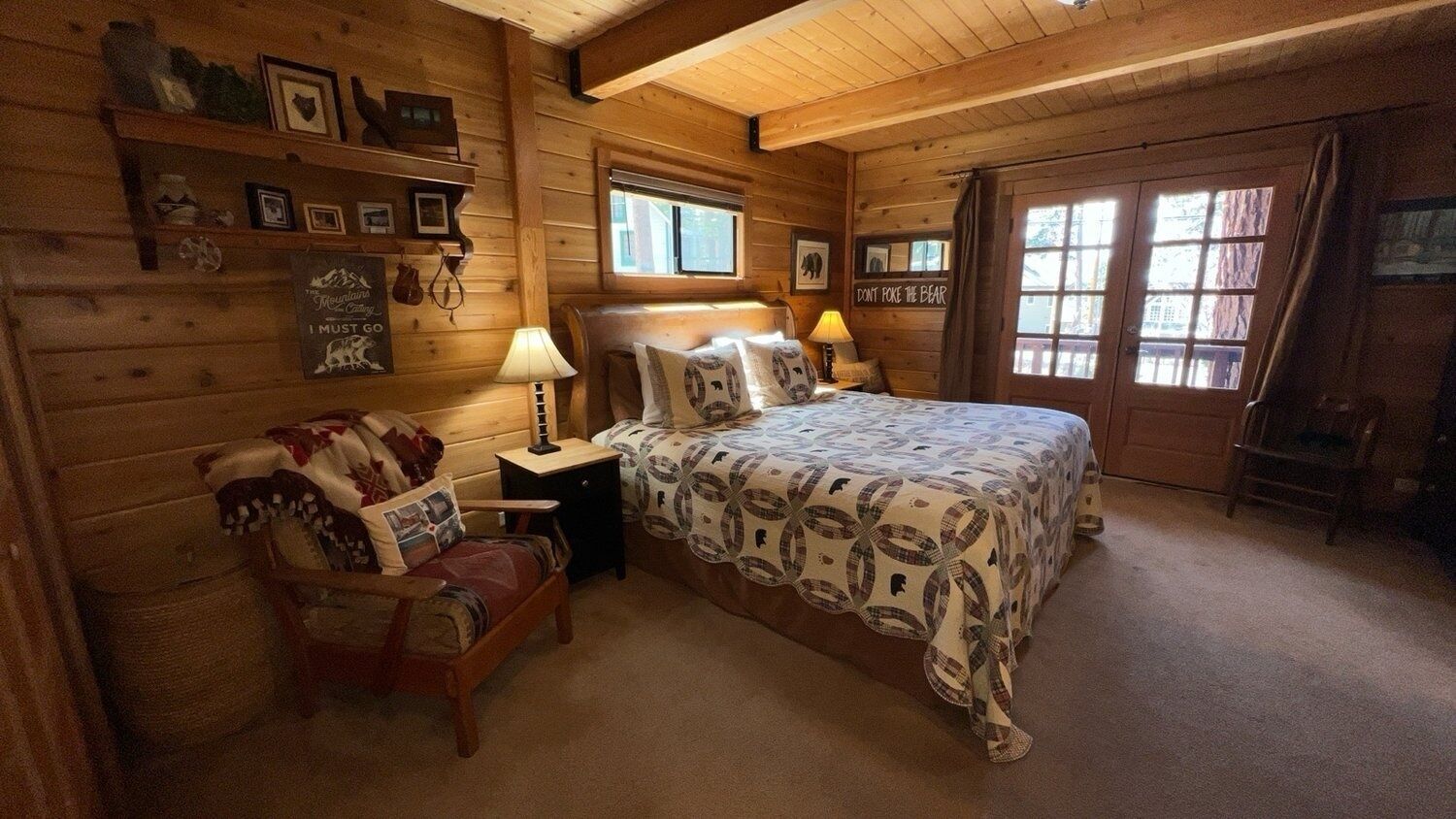 A cozy log cabin room with a large bed, a chair, a nightstand, and a window with curtains.