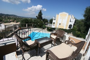 A rooftop terrace with wicker furniture, a swimming pool, and a view of the surrounding landscape.