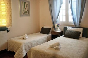 A hotel room with two beds, a nightstand, a painting, and a window with curtains.