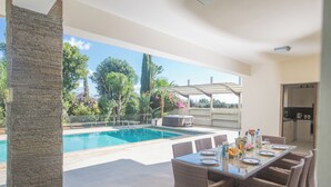 Een eetgedeelte bij het zwembad met uitzicht op het zwembad, omringd door weelderige begroeiing en een pergola.