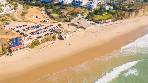 An aerial view of a beach with a parking lot, buildings, and a small beachside restaurant. - Modern villa near beach [86] (Lagos)