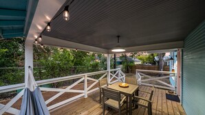 Terraza cubierta al aire libre con una mesa y sillas, rodeada por barandilla blanca y piso de madera.