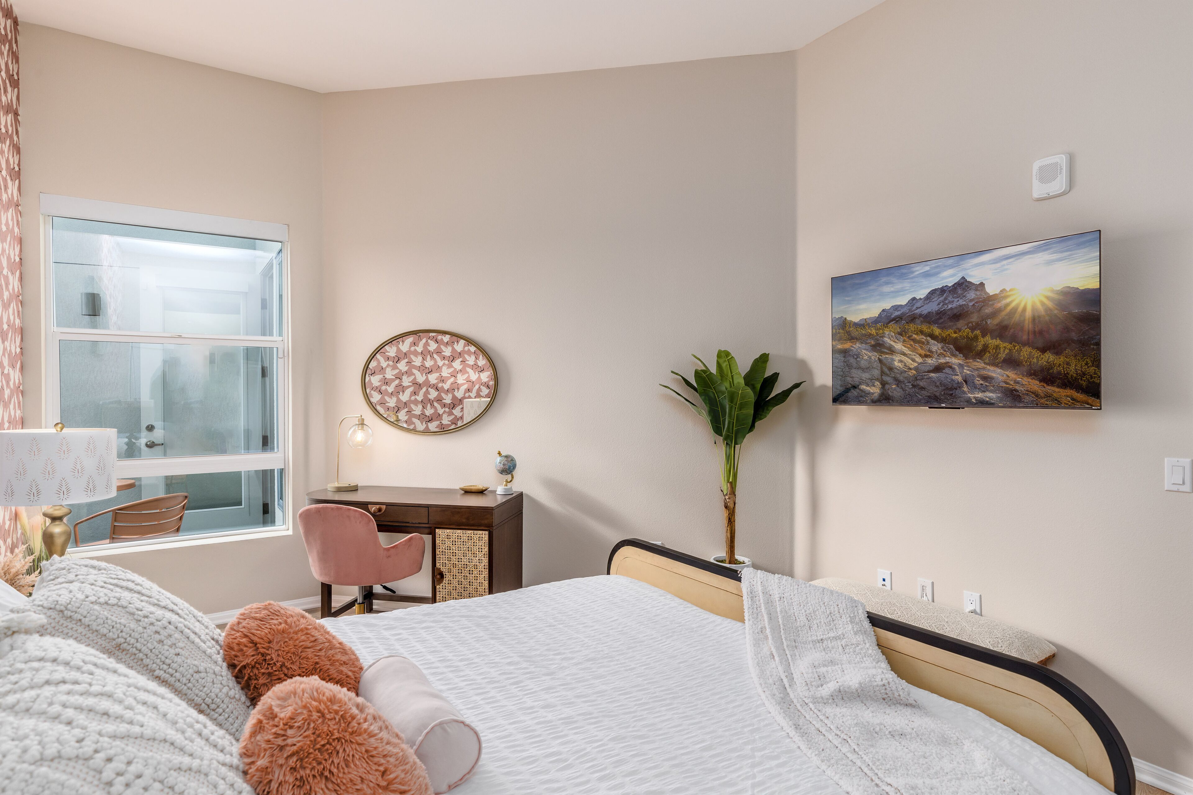 Un dormitorio con cama, escritorio, silla, ventana y un cuadro colgado en la pared.