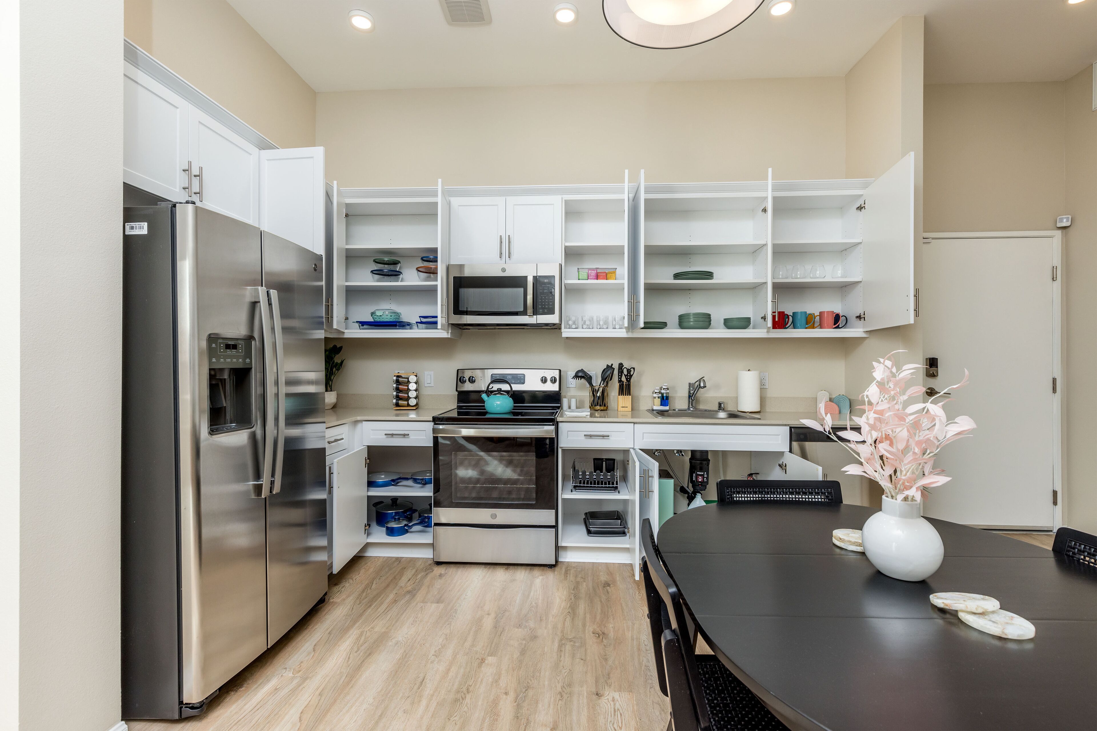 A modern kitchen with stainless steel appliances, white cabinetry, and a dining area with a vase of flowers.