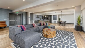 A modern living area with a grey sectional sofa, a round wooden coffee table, and a patterned rug. - Eclectic : 65” TVs : Fast Wi-Fi : Parking : Pets : Bohemian (San Diego)