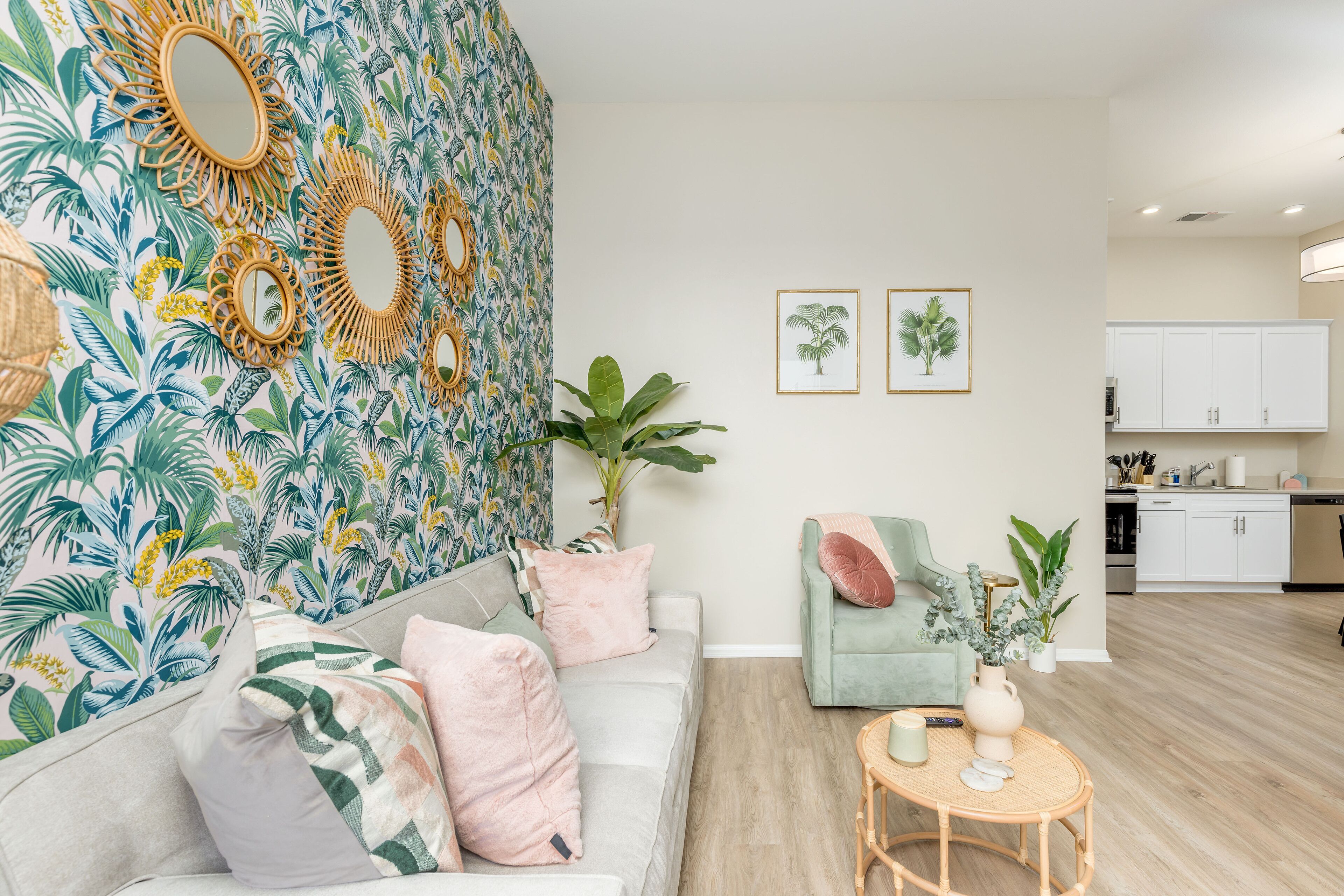 A living room with a sofa, armchairs, a coffee table, and a wall with tropical wallpaper and mirrors.