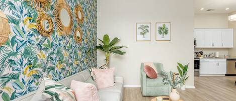 A living room with a sofa, armchairs, a coffee table, and a wall with tropical wallpaper and mirrors.