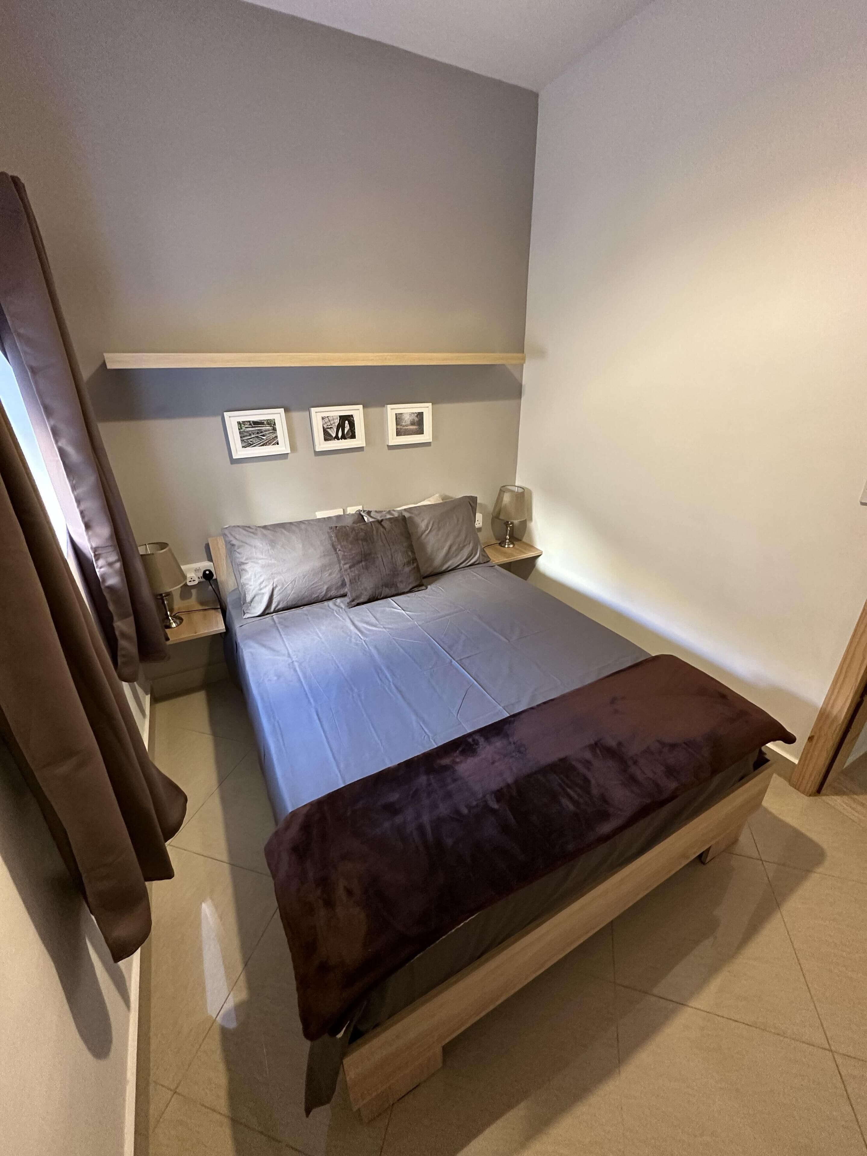 Une chambre à coucher avec un lit, une table de chevet, une lampe et trois tableaux encadrés accrochés au mur.