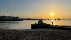 A beach with a person fishing near a breakwater, boats in the water, and buildings in the background. - Ewa Apt - 3-bed Near Sliema - St Julians Seafront (Gzira)