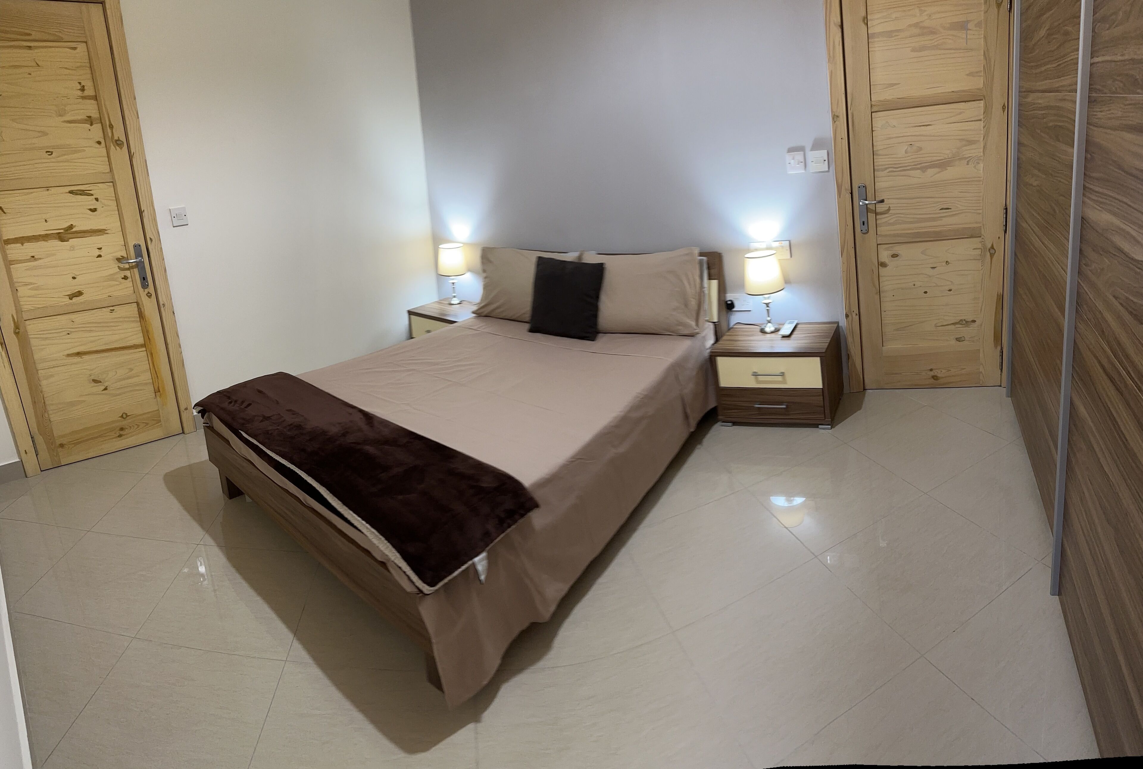 Een keurig opgemaakte slaapkamer met een bed, nachtkastjes en houten kledingkasten.