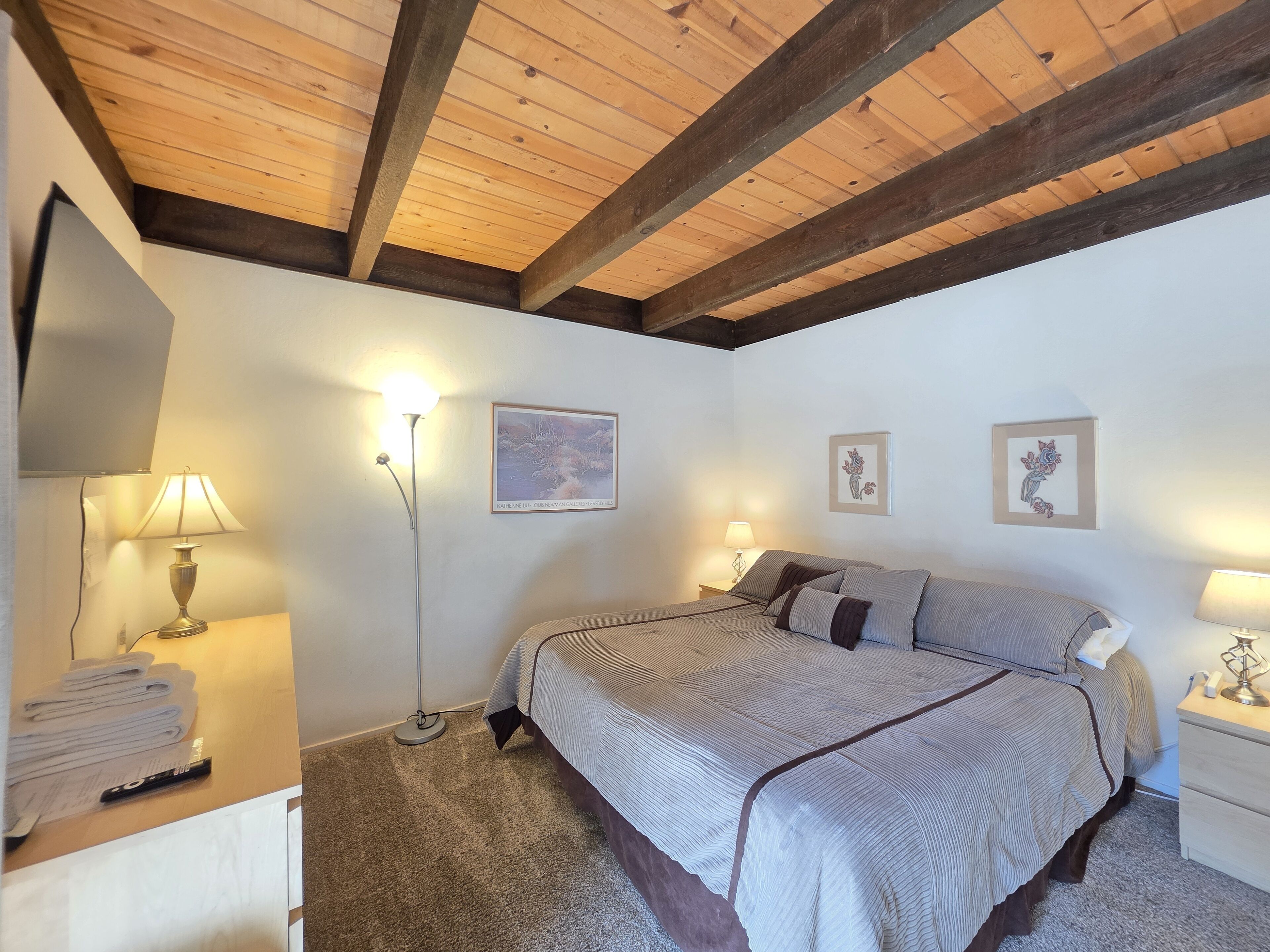 A bedroom with a bed, two bedside tables, a floor lamp, and wall art.