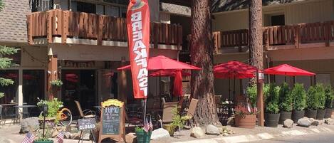 A restaurant with outdoor seating, red umbrellas, and a flag.