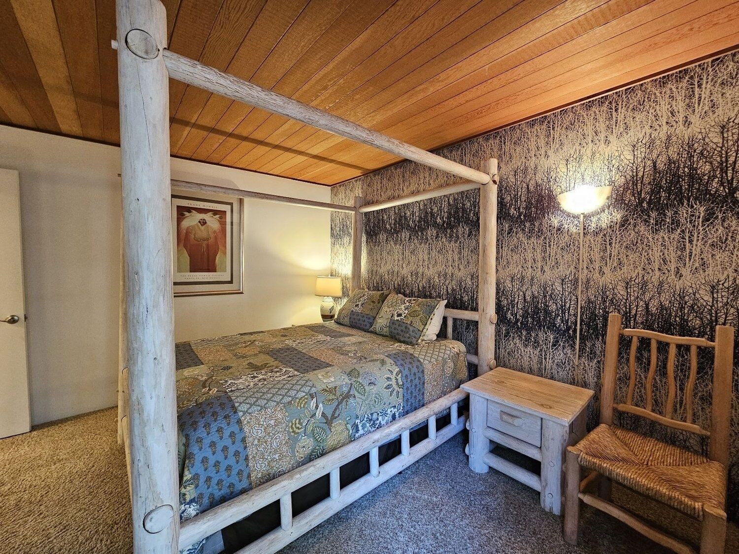 Un llit amb cortines, un estriat, una cadira i una làmpada penjada a la paret.
