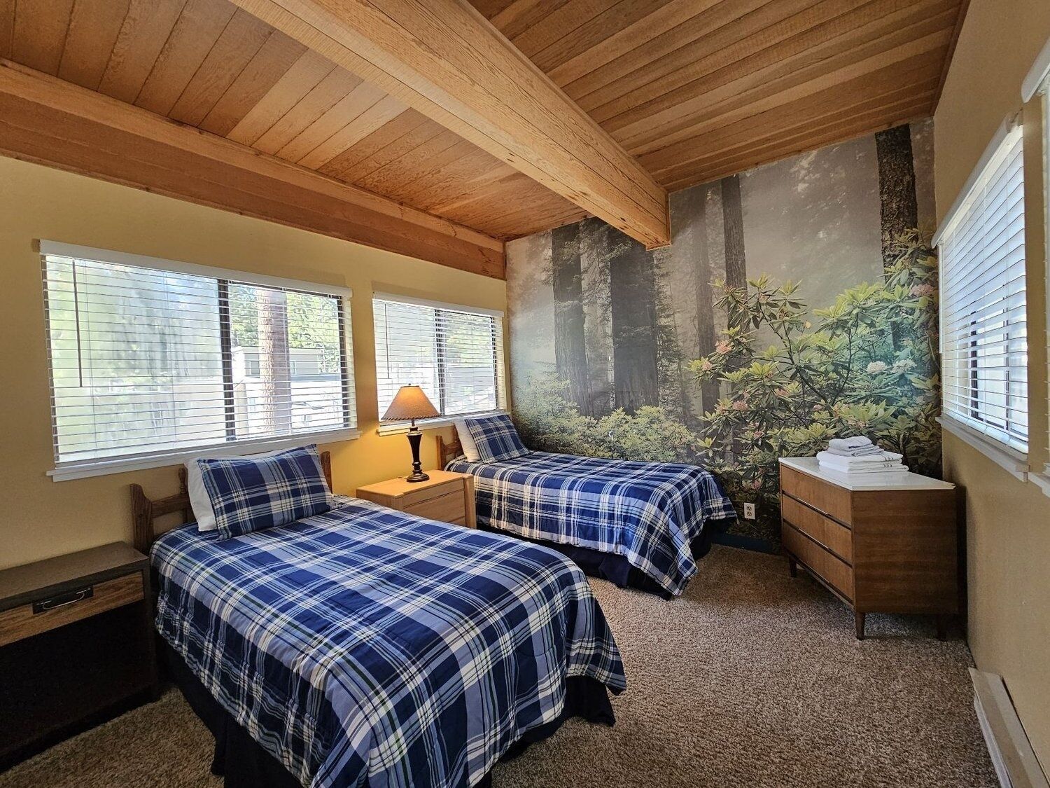 Un dormitorio con dos camas, una mesita de noche, un aparador y un mural de un bosque en la pared.
