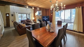 Un salón amplio con techo de madera, comedor con mesa y sillas de madera, chimenea y televisor.