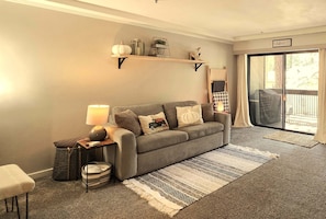 A living room with a grey sofa, a lamp, a small table, a basket, and a rug.