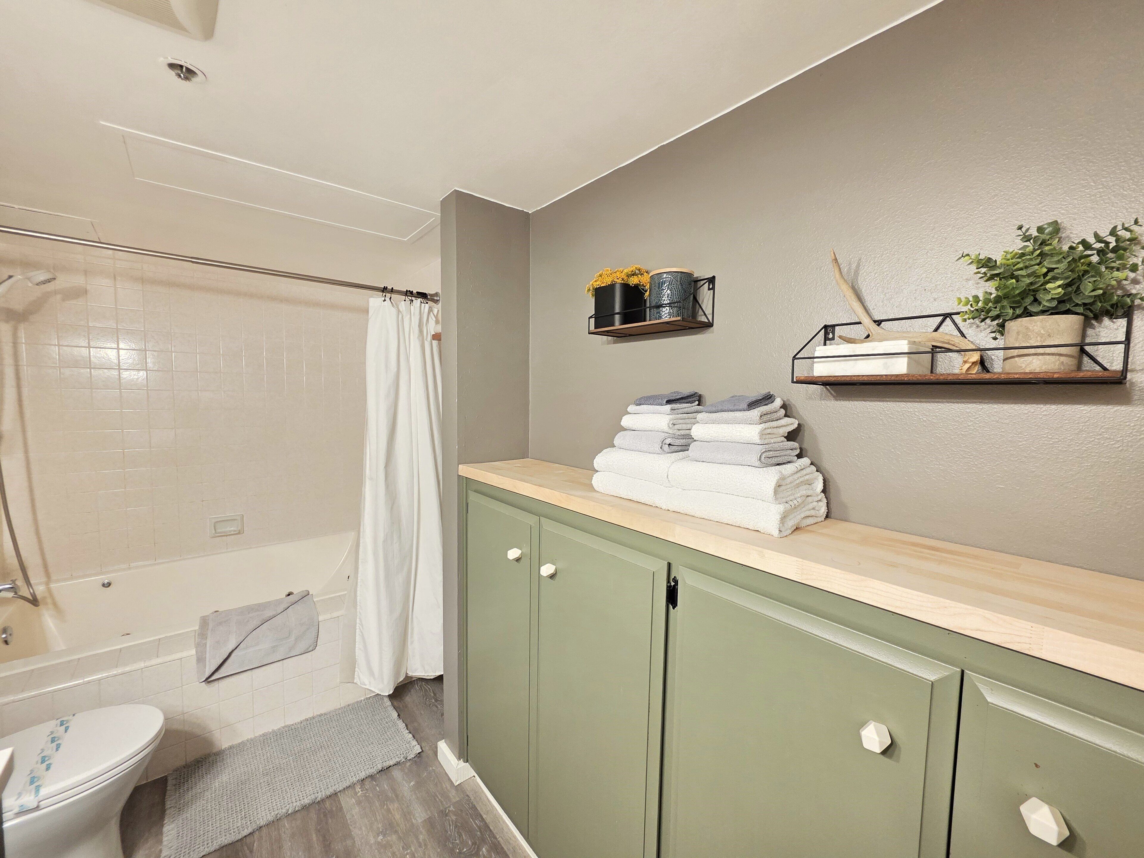 A bathroom with a shower, toilet, green cabinets, and a towel rack with folded towels.