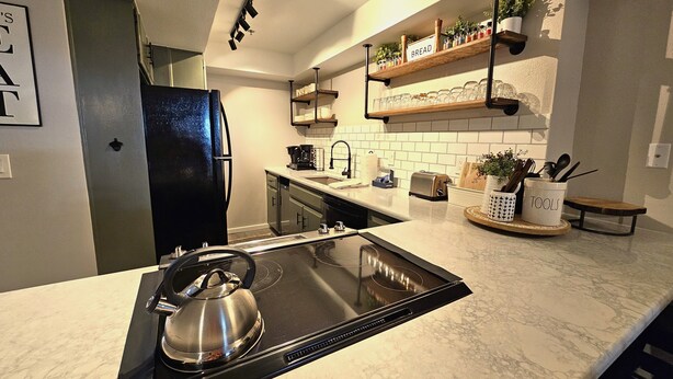 A modern kitchen with a black induction cooktop, a stainless steel kettle, a toaster, and a coffee maker. - Taste Of Burgundy 1 Bedroom Condo by RedAwning (Incline Village)