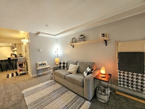 Un salon avec un canapé, une lampe, un tapis et une étagère fixée au mur.