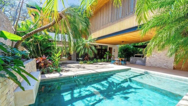 Una piscina rodeada de exuberante vegetación y una pérgola de madera.